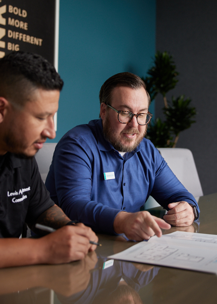 Two men sitting at a table, focused on a piece of paper. They seem engaged in a discussion or working together on a project.