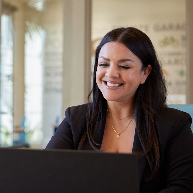 A woman smiling while using a laptop computer to work on a project.